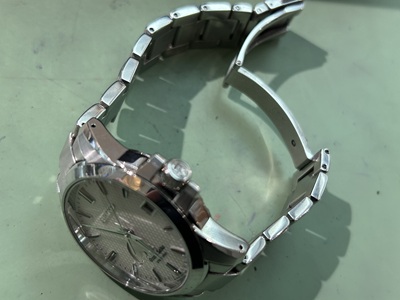 職人が精密なハンマーとピンを使い、バックルを組み立てている指先のアップ。