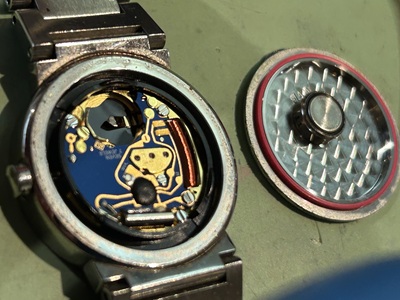 裏蓋が外され、銀色のムーブメントと電池が露出した様子。