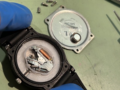 裏蓋が外され、内部の銀色のムーブメントと小さなボタン電池が見えている状態。