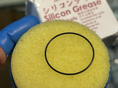 黄色の台の上で、ゴムパッキンに透明なシリコングリースを均一に塗布している。