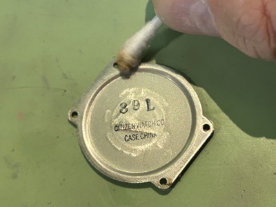 取り外された金属製の裏蓋の裏側を、綿棒を使って磨き上げている。