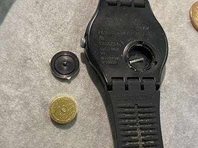 取り外された黒い裏蓋と、金色のボタン電池。