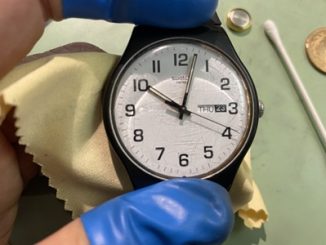 青い指サックをつけた職人が、時計を丁寧に拭き上げている様子。