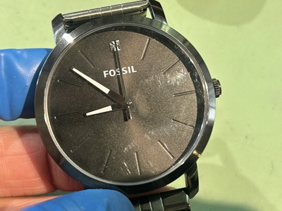 FOSSILの大きな文字盤の腕時計を指サックをした手で持っている様子