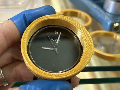 時計の周りにぴったりとはまった、3Dプリンタ製の黄色い円形の工具