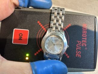 裏蓋が閉じられたグッチの腕時計が、緑色のランプが点灯する「パルスチェッカー（回路検知器）」の上に置かれている様子。
