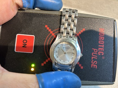 裏蓋が閉じられたグッチの腕時計が、緑色のランプが点灯する「パルスチェッカー(回路検知器)」の上に置かれている様子。