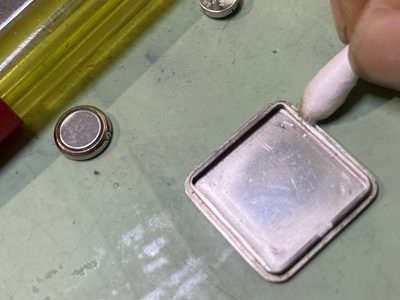 外した時計の裏蓋の縁に溜まった黒い汚れを、綿棒で丁寧に取り除いているメンテナンス風景。