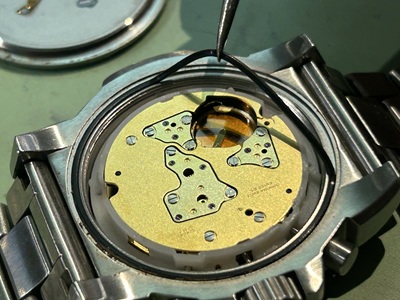 裏蓋の溝から、防水の要である黒い輪状のゴムパッキンをピンセットで優しく取り剥がしている様子。