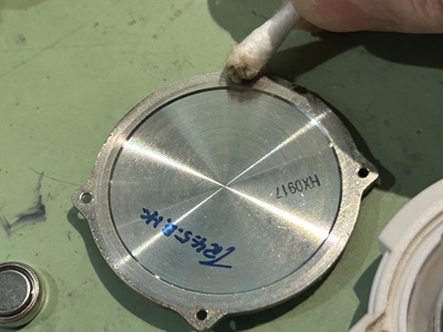 取り外した金属製の裏蓋の裏面やネジ穴周辺を、綿棒で丁寧に磨いて汚れを落としている写真。