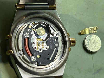 非常に小さなレディース仕様のムーブメントから、ピンセットを使って古いボタン電池を慎重に浮かせ、取り除いている瞬間。
