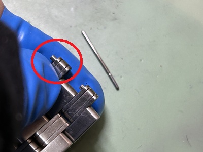 ピン留め工具を使い、金属ベルトのコマの内部に非常に小さな固定用パイプパーツ(Cリング)を丁寧に仕込みながら、連結ピンを元の位置へ打ち込んでベルトを再結合している手元の作業。