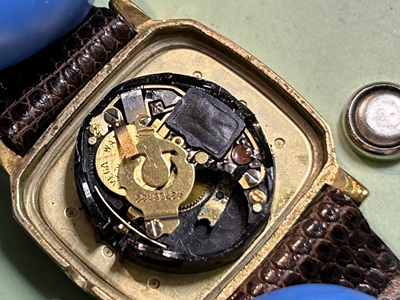 ピンセットを使い、ムーブメント中央の格納スペースから古いボタン電池を取り除いている手元。