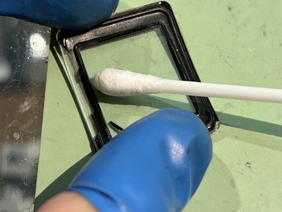 工具やクロスを用いてガラス内側の接着面をきれいに拭き取り、固着した古い固定剤を慎重に取り除く作業風景