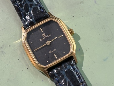ゴールドカラーの丸角型ケースに、黒い文字盤のクラシカルなウォルサム(WALTHAM)のレディース腕時計。