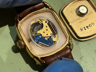 開封されたハミルトンの腕時計本体のムーブメントと取り外された金色の裏蓋