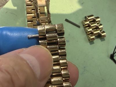 時計修理用の専用工具を使いメタルバンドのサイドから慎重にピンを抜いている作業風景