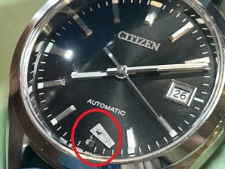 文字盤の6時位置から剥がれ落ちて転がっているインデックスパーツ（赤丸で強調）