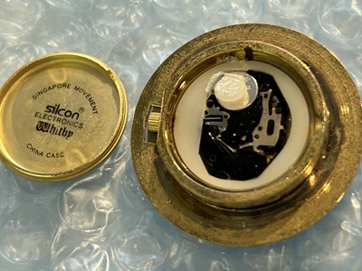 外された裏蓋(silcon ELECTRONICS Whitby CHINA CASEの刻印)の横で、内部のクォーツムーブメントと白い液漏れサビの結晶が露出している様子