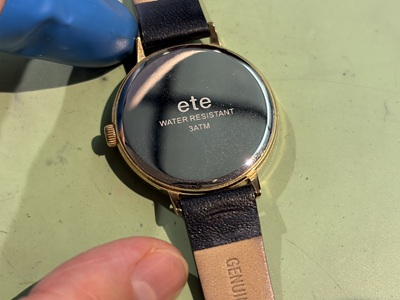 eteの腕時計を裏返し、ゴールドの裏蓋に「ete」「WATER RESISTANT 3ATM」と刻印されている様子