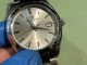 青い指サックをはめた手で大切に持たれた、グランドセイコー（Grand Seiko）のクォーツ式腕時計。気品あるシルバーのサンレイ文字盤に、シャープなドルフィン針とインデックス、3時位置に日付窓（14日表示）が配置されている美しい時計の画像。