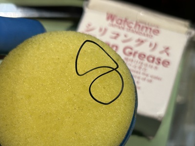 イエローのグリース塗布用スポンジの上に置かれた黒い裏蓋パッキン