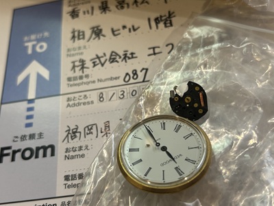 宅配便の伝票の上に置かれたウェッジウッドの時計本体と外れたムーブメントパーツ