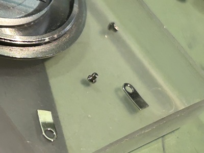 トレイに置かれたムーブメント固定用の極小ネジと爪パーツ