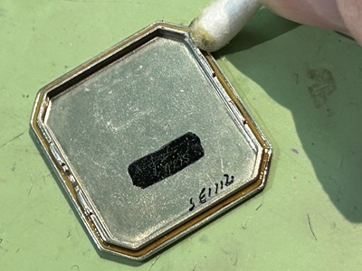 八角形の裏蓋プレートのフチを綿棒で丁寧に清掃している作業