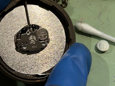 裏蓋を開け、内部の超小型ムーブメントから古い電池を取り除き、綿棒で清掃する様子