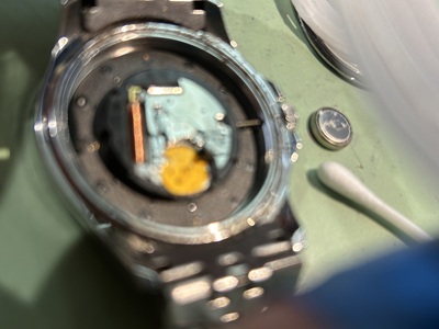古い電池を取り外し、ムーブメント周辺の汚れを綿棒で清掃している手元