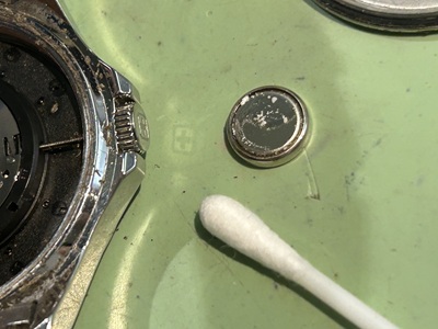 外した電池の粉吹き・液漏れ痕とケース外周の汚れを綿棒で清掃する様子