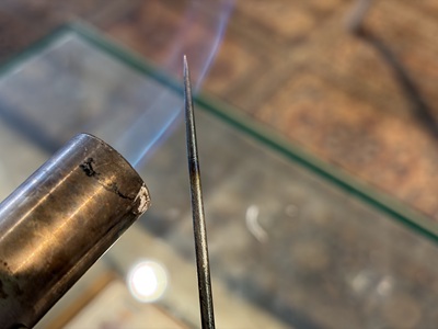 バーナーの青い炎で先端の鋭利な金属工具を熱している作業風景