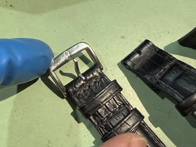 新しい革ベルトに移植・固定されたオメガの専用尾錠を指で押さえて点検している様子
