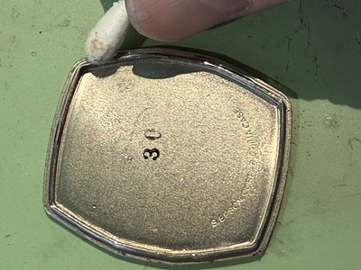 取り外した裏蓋の内側溝に溜まった固着汚れを綿棒で清掃する作業